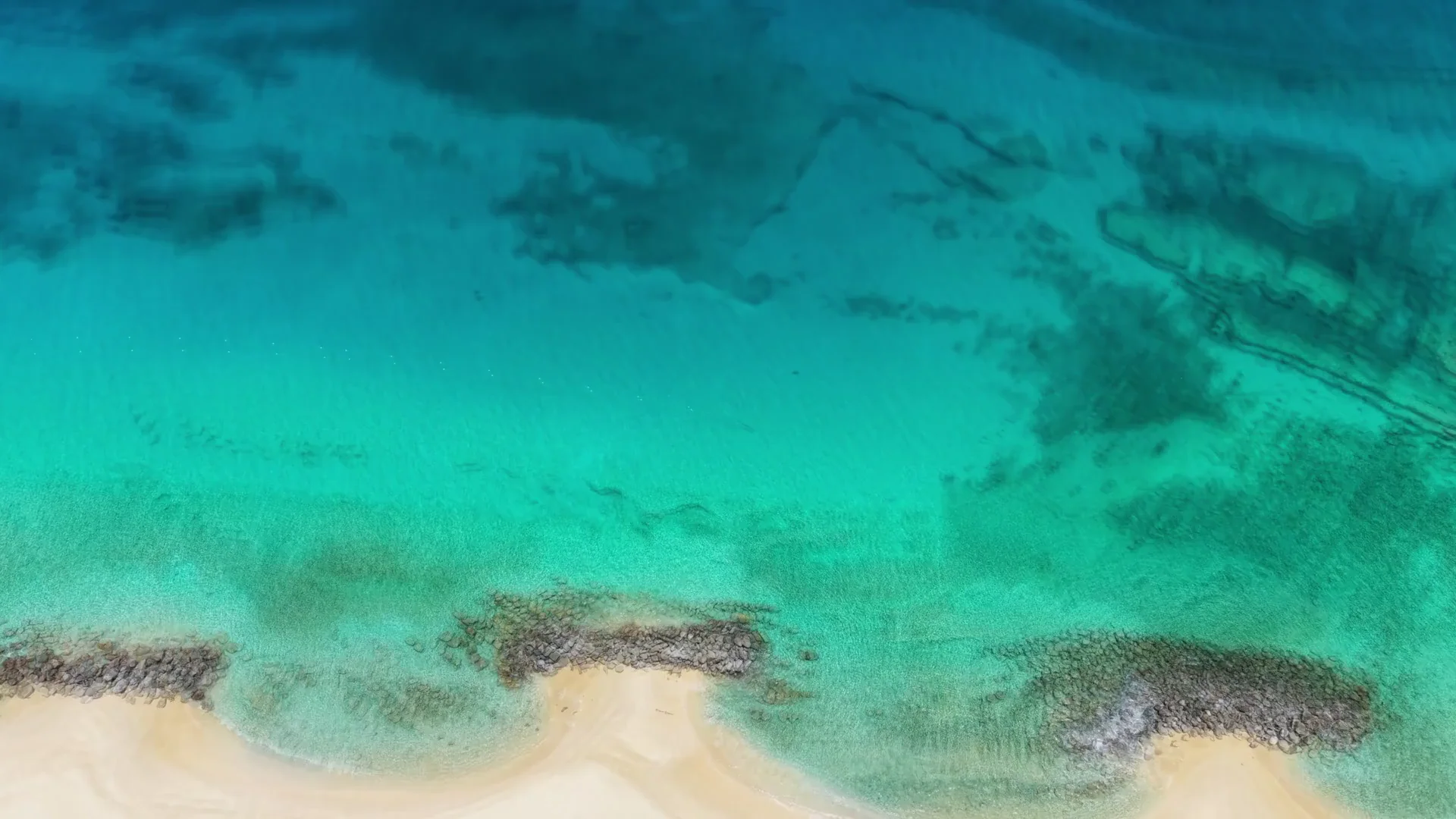Vista aérea do mar turquesa com ondas suaves junto à faixa de areia