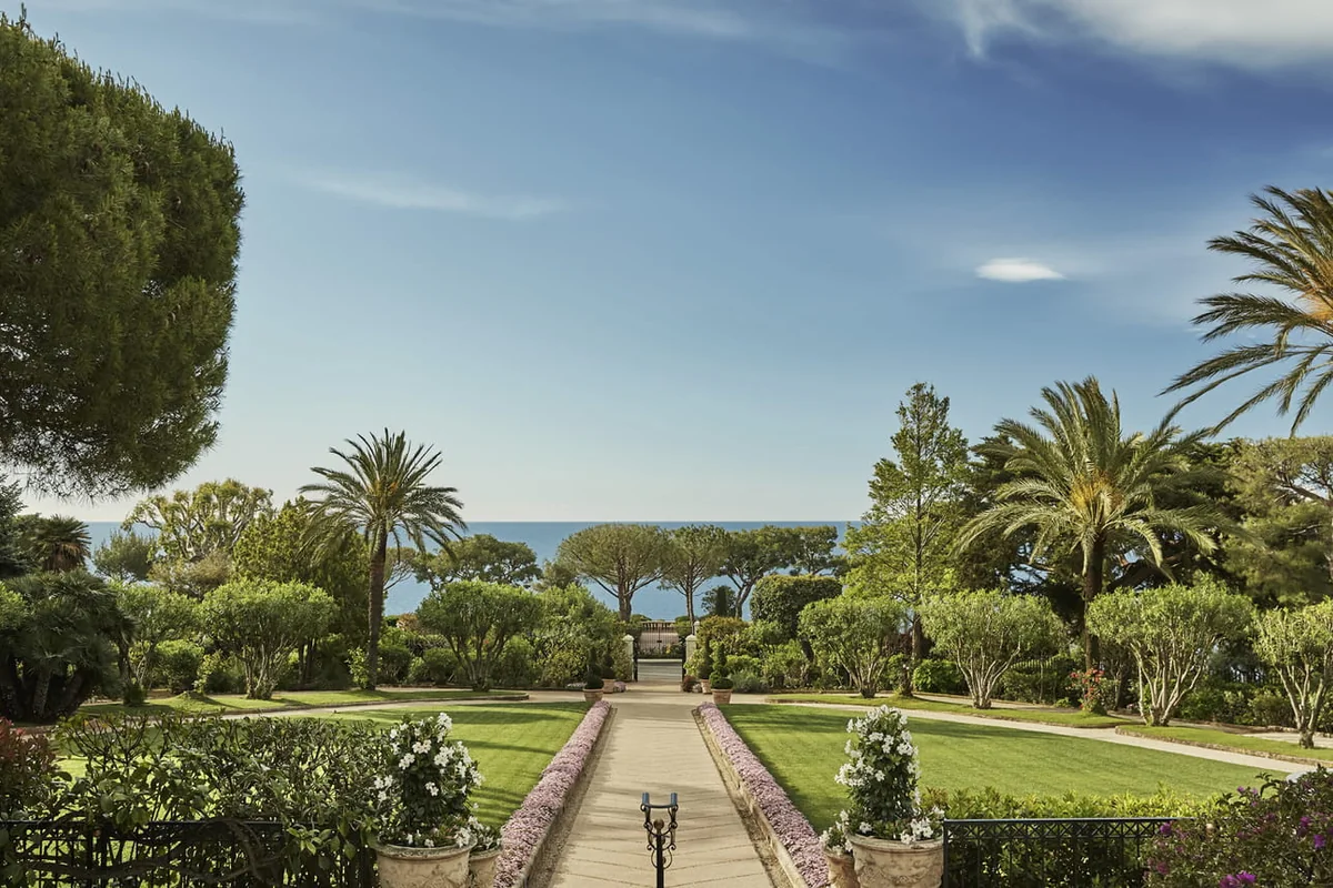Caminho entre jardins e palmeiras com vista para o mar