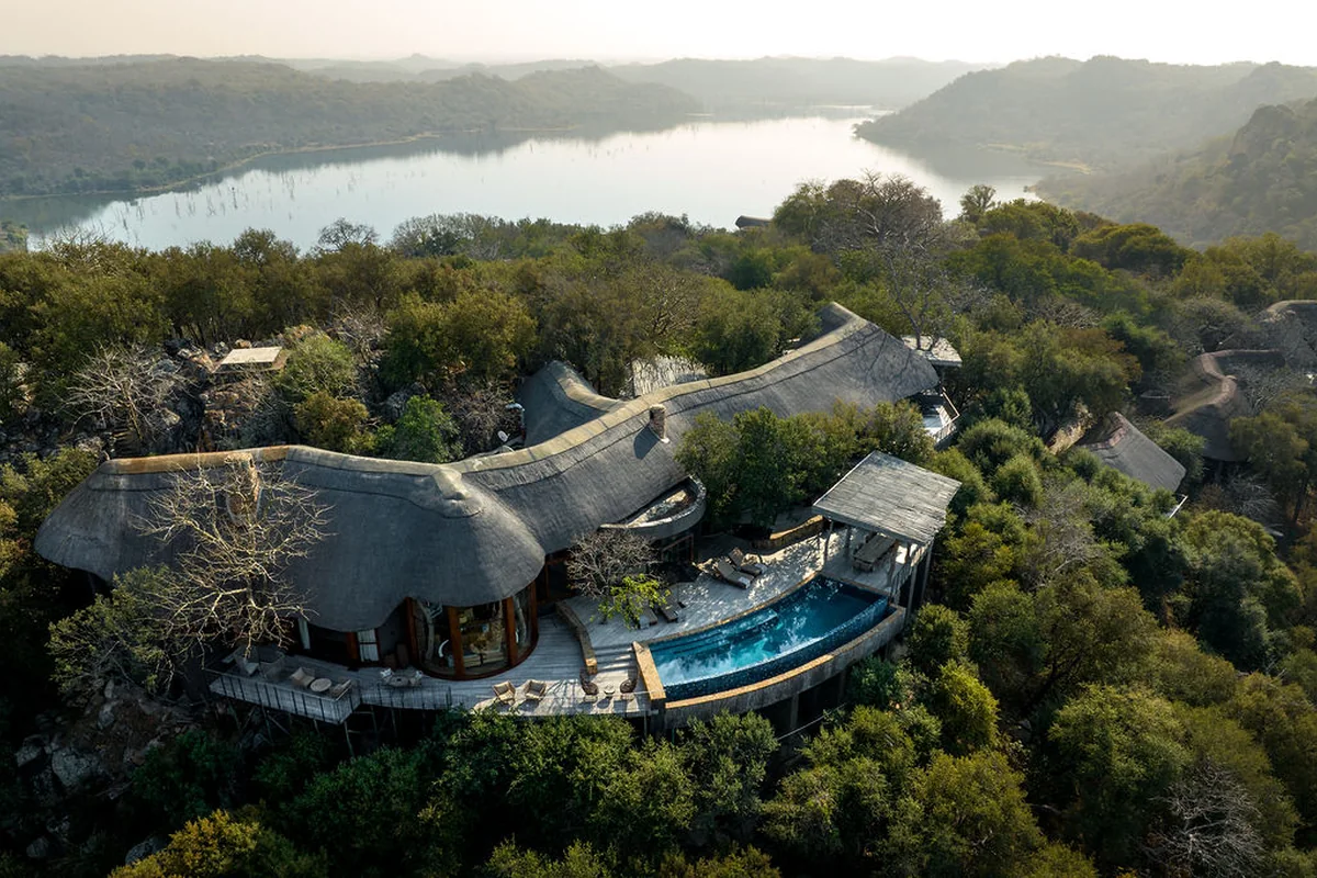 Vista aérea de um lodge com piscina curva cercado pela vegetação e próximo a um rio